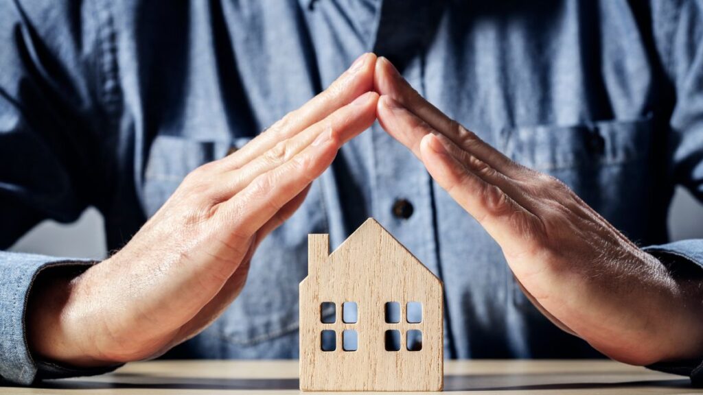manos encima de una casa pequeña de madera