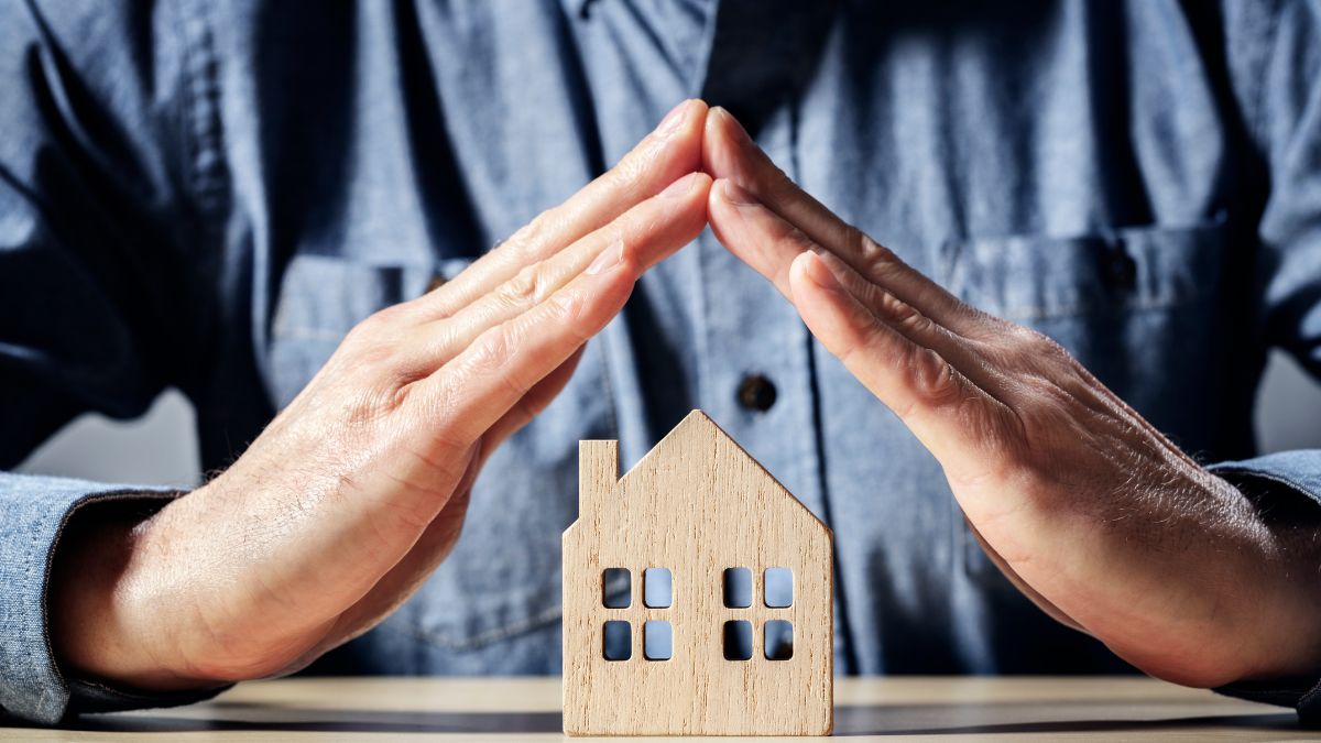 manos encima de una casa pequeña de madera